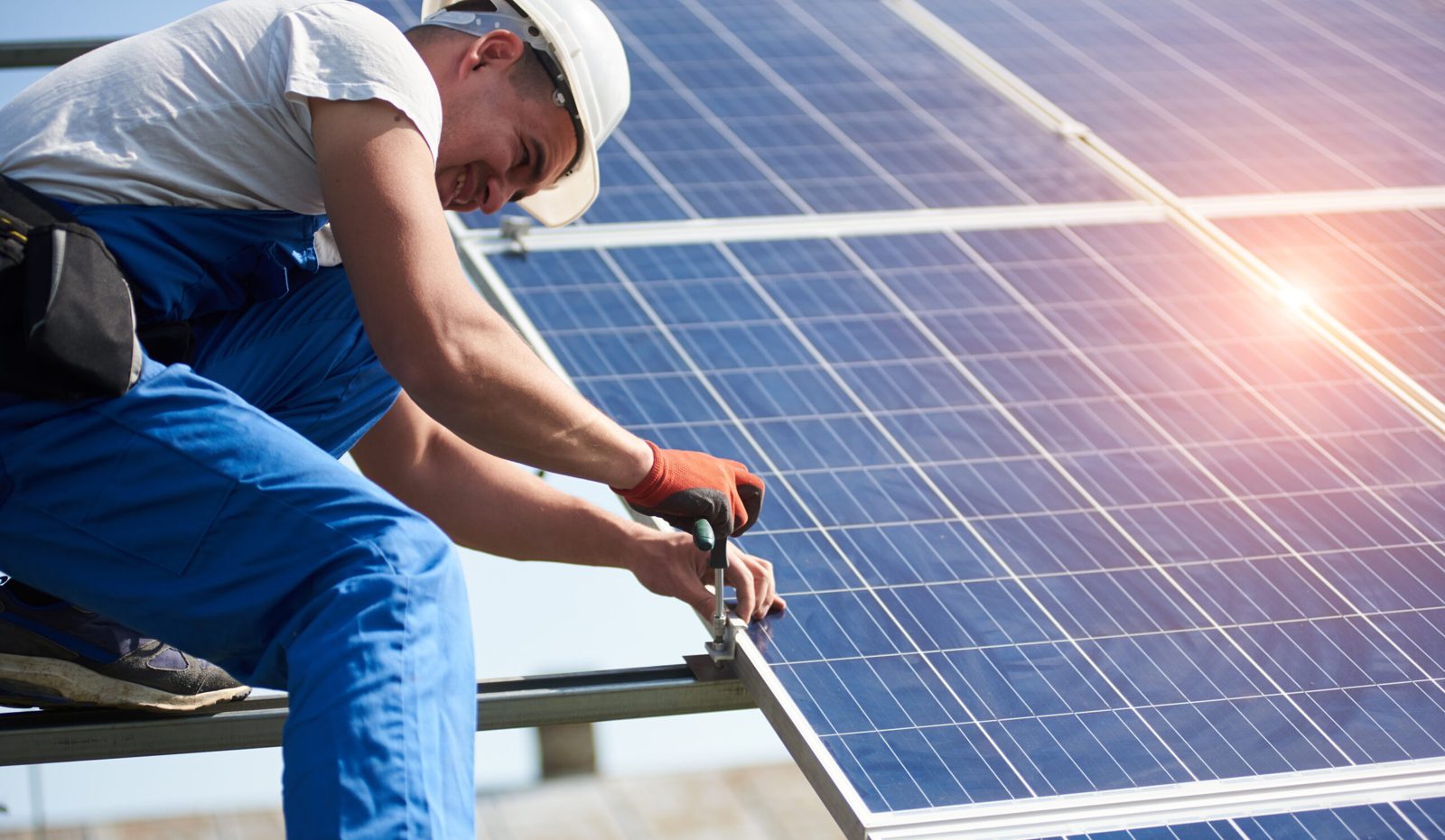 Installer in a hard hat tightening a clamp that holds a solar panel to its rail